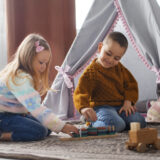 Kaks last mängivad toas telgi ees puidust mänguasjadega põrandal